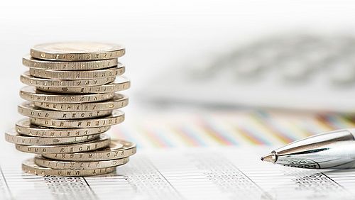 Ein Symbolbild Münzen und ein Stift